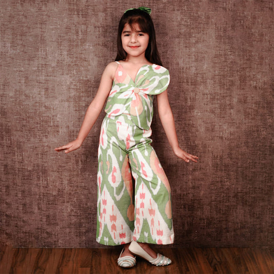 Young girl wearing a green floral dress against a brown textured wall.