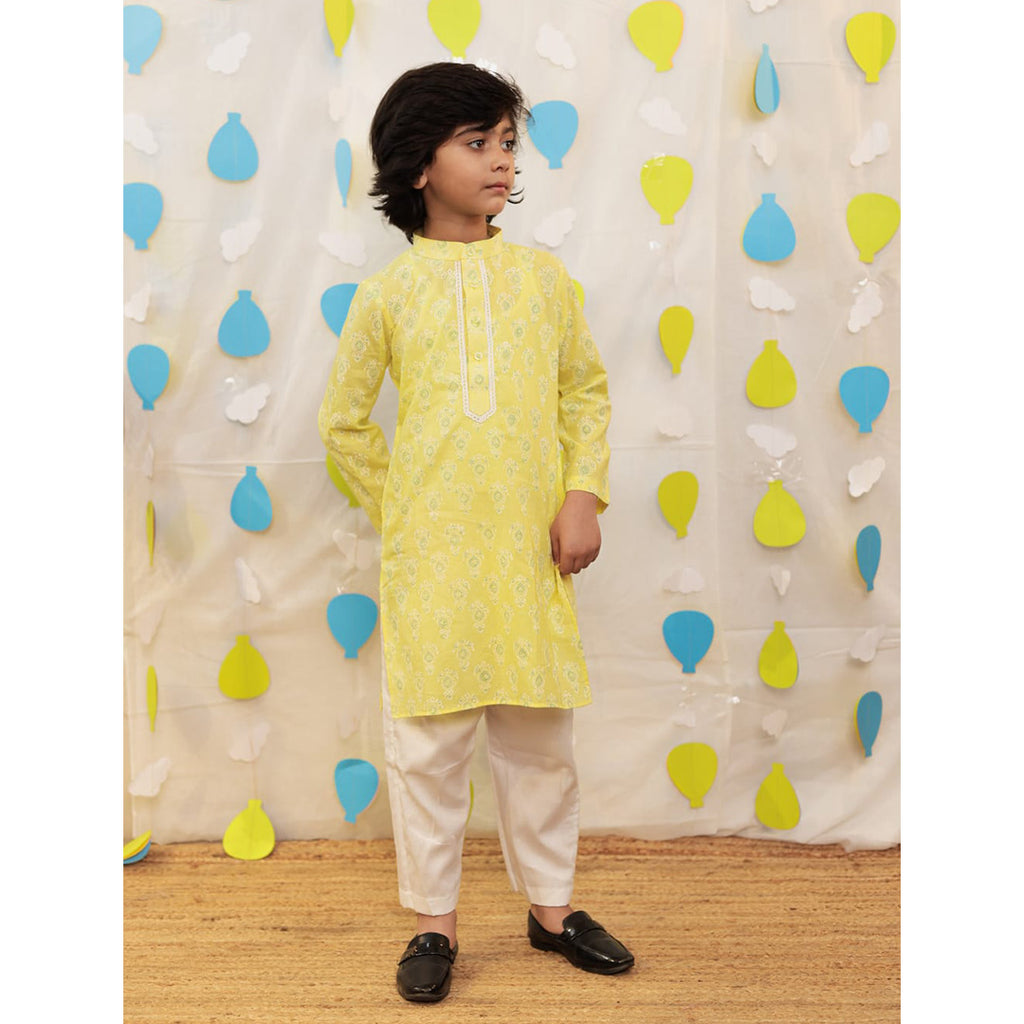 A boy wearing a yellow kurta with white pants.